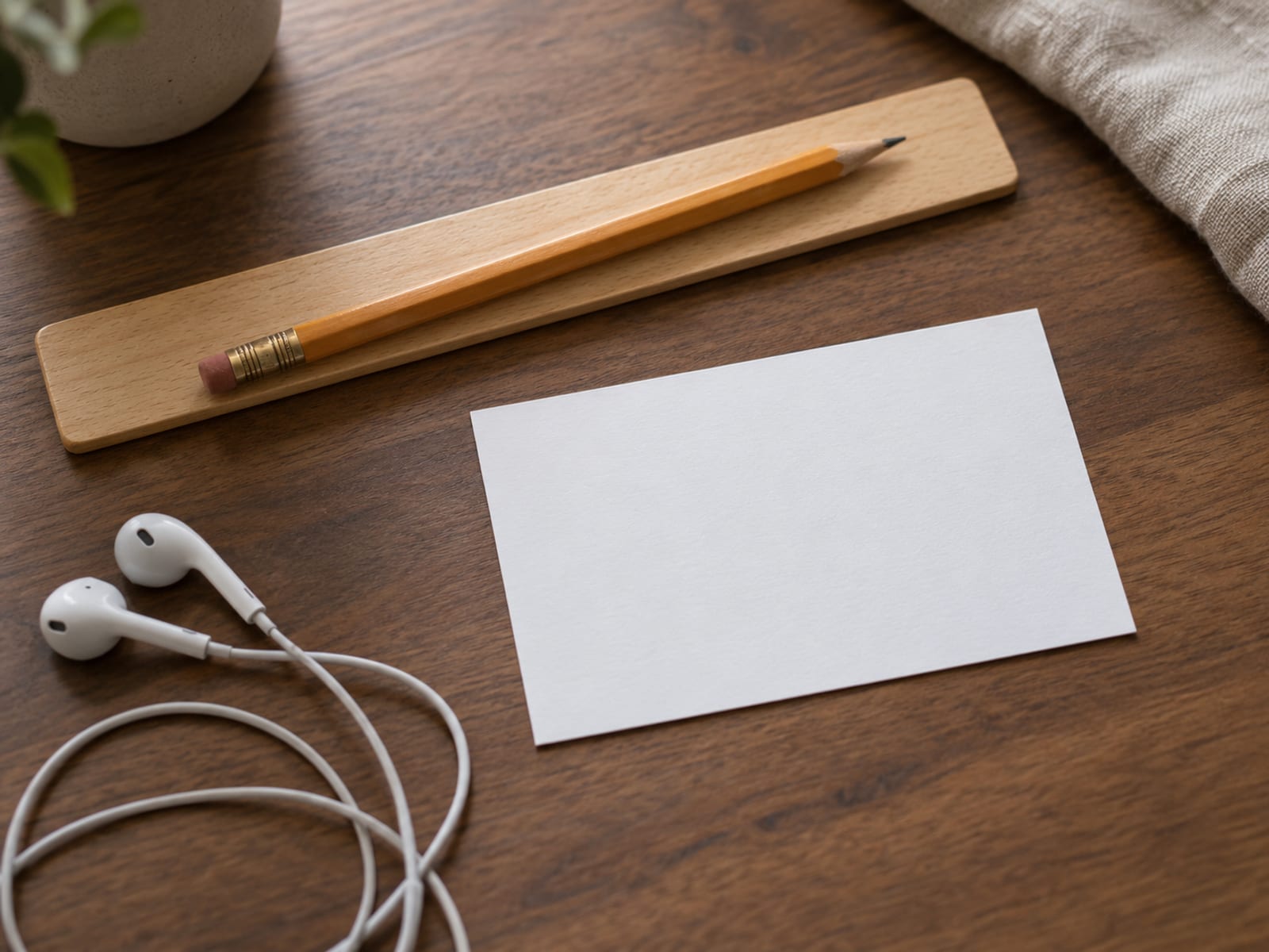A wooden ruler, a pencil and a blank index card laid out on a desk beside a pair of plain earbuds.