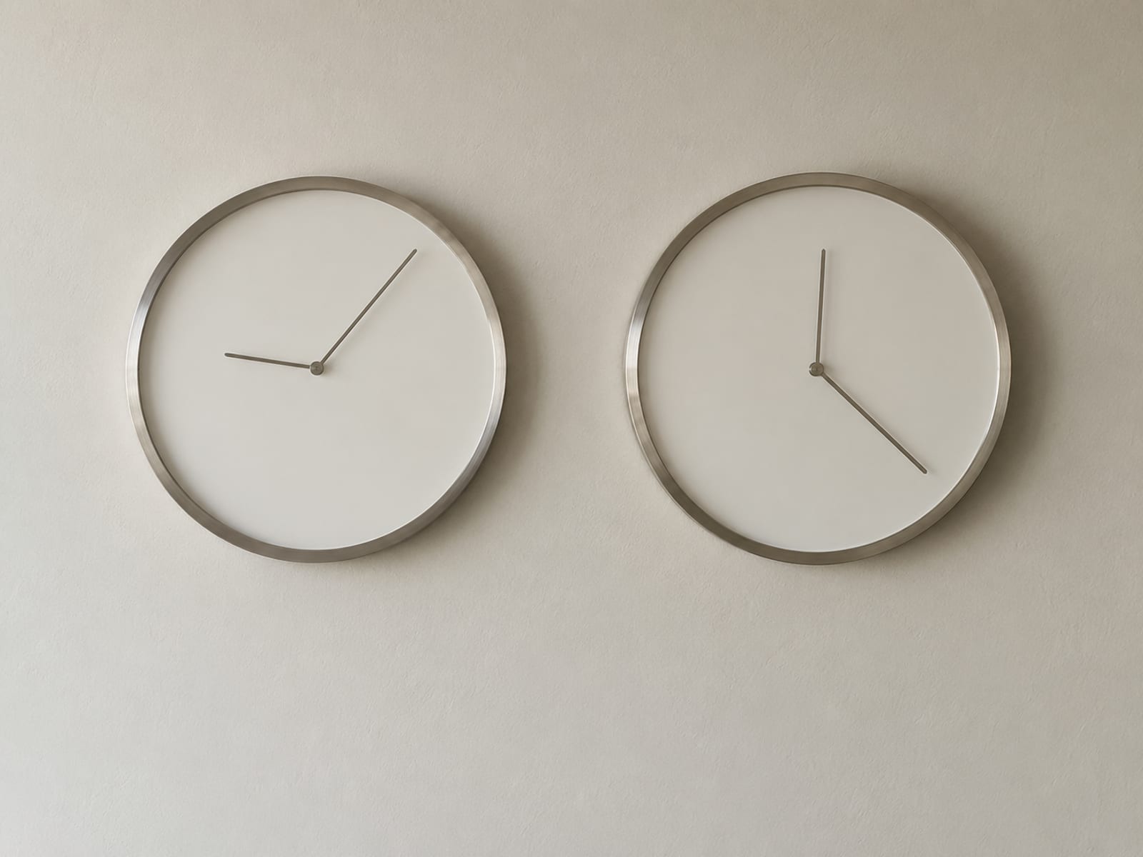 Two round analogue wall clocks with blank faces hanging side by side on a pale wall, their hands showing different times.