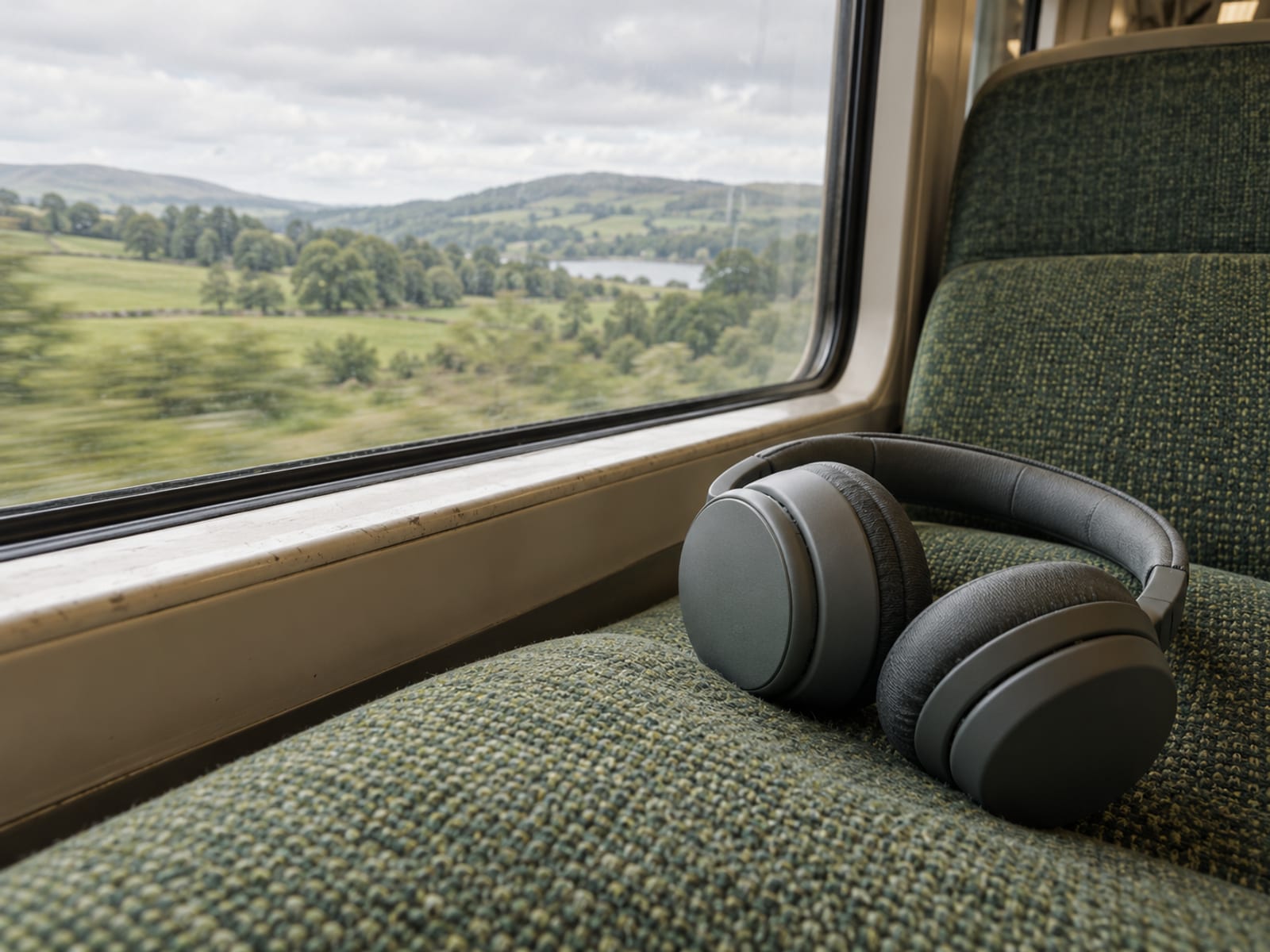 A long train window seat with a pair of headphones resting on the cushion and blurred countryside outside the window