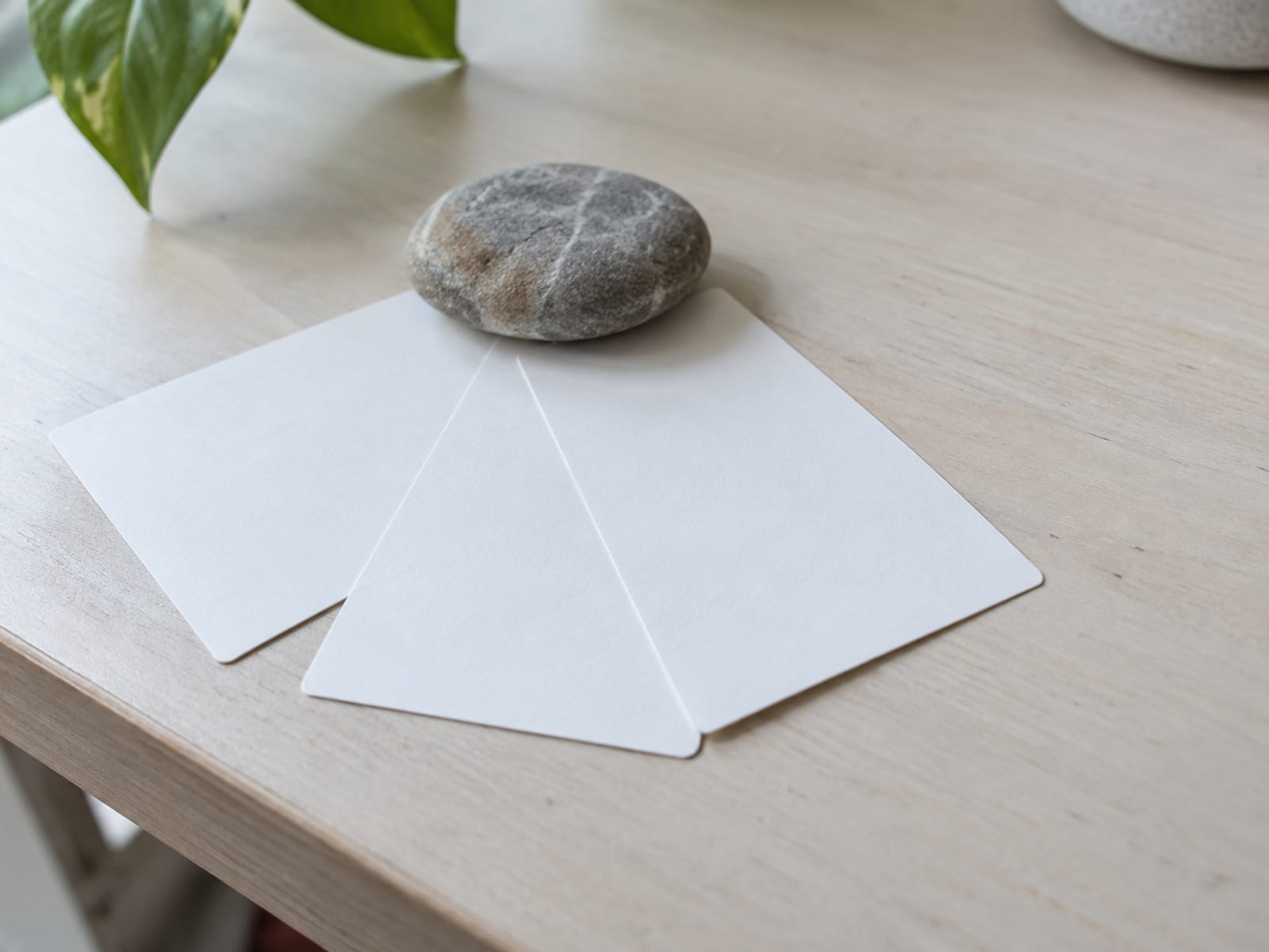 Three blank index cards fanned on a desk with a smooth grey river stone resting on top of them.