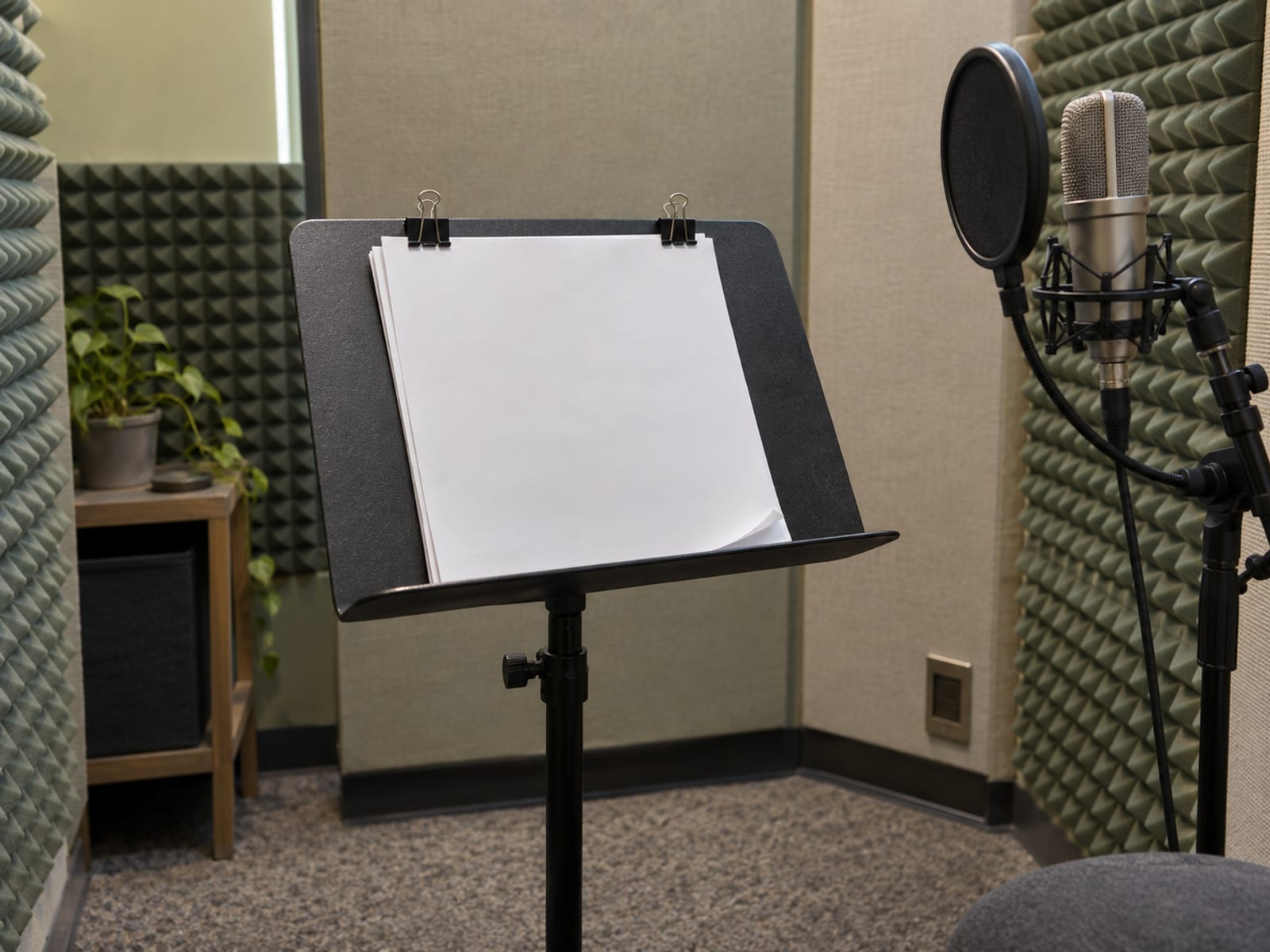 A quiet recording booth with blank manuscript pages clipped to a music stand in front of a microphone-free padded wall